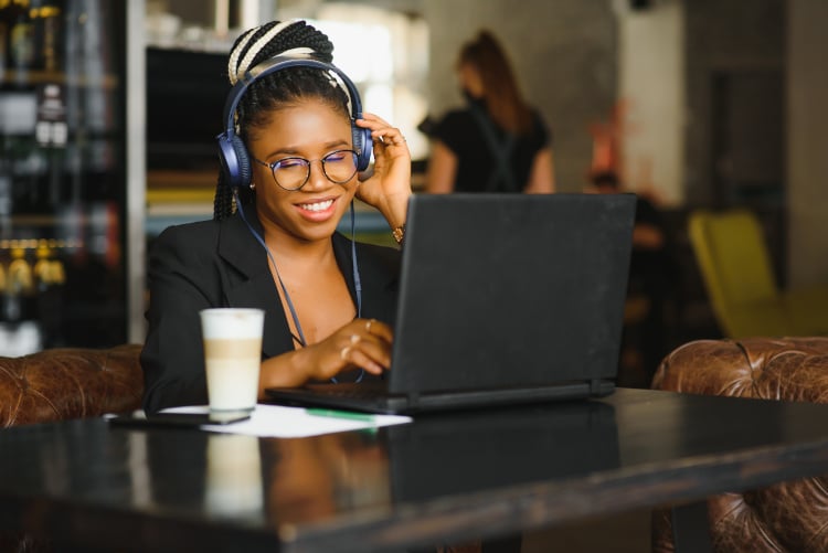 Smiling woman with headphones and laptop communicating with clients and customers in a cafe