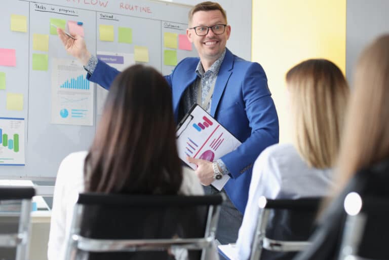 Smiling facilitator sales trainer helping two salespeople in a workshop training room